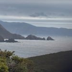 Misty Australian coastline with rock formations sharp in the foreground fading into a hazy, indistinct headland in the distance