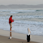 Man fishing on a quiet Australian beach at dawn with a pelican and seagull nearby — a calm coastal scene symbolising observation, stillness, and emotional awareness.”